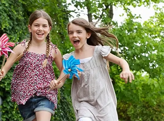 Two young girls running outside with toy pinwheels in their hands