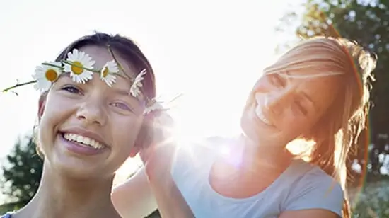 Mujer poniéndole una corona de flores a una niña, al aire libre