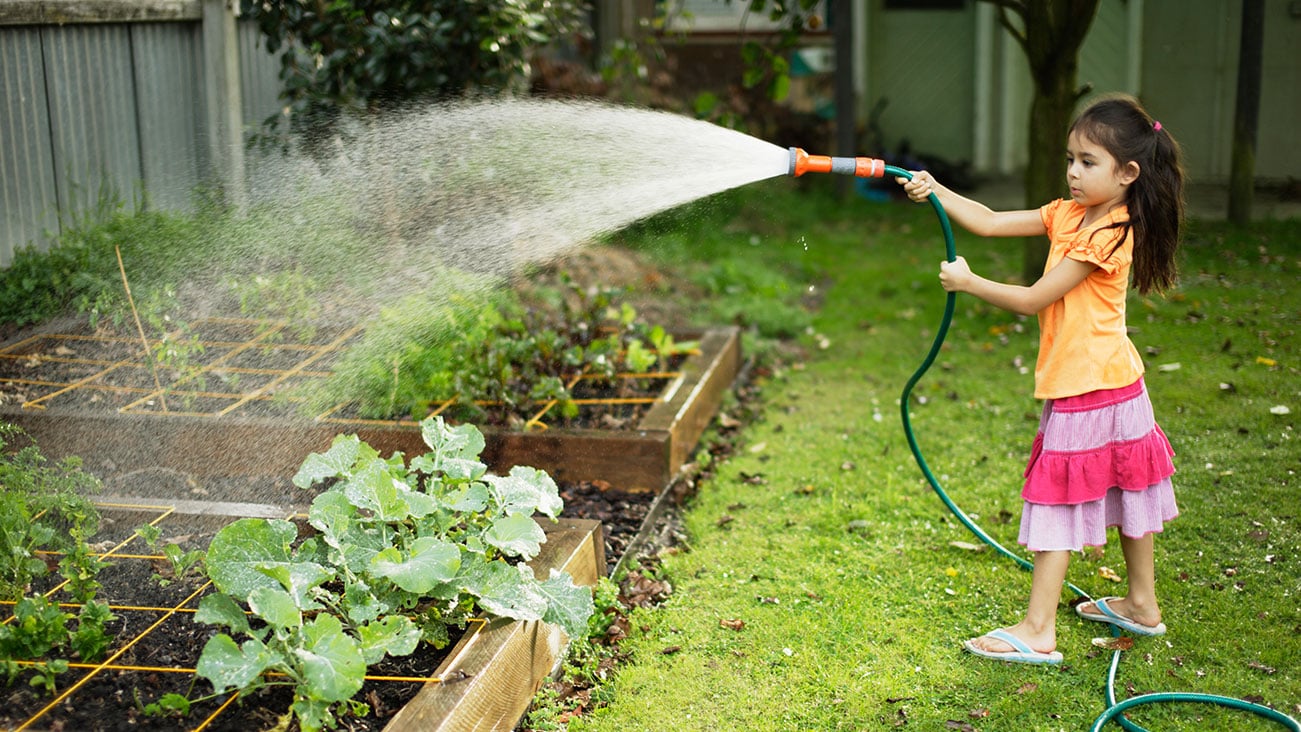 Child holding a hose to water the garden
